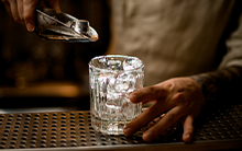 Closeup of Bartender with a tattoo adding ice to a glass