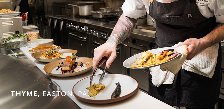 Chef plating gourmet dishes in a commercial kitchen at Thyme restaurant in Easton, PA, with several prepared plates of food arranged on the counter.